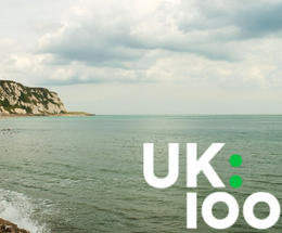 An image of the UK100 logo against the Folkestone coastline