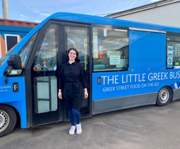 Business owner standing in front of her mobile food van called The Little Greek Bus