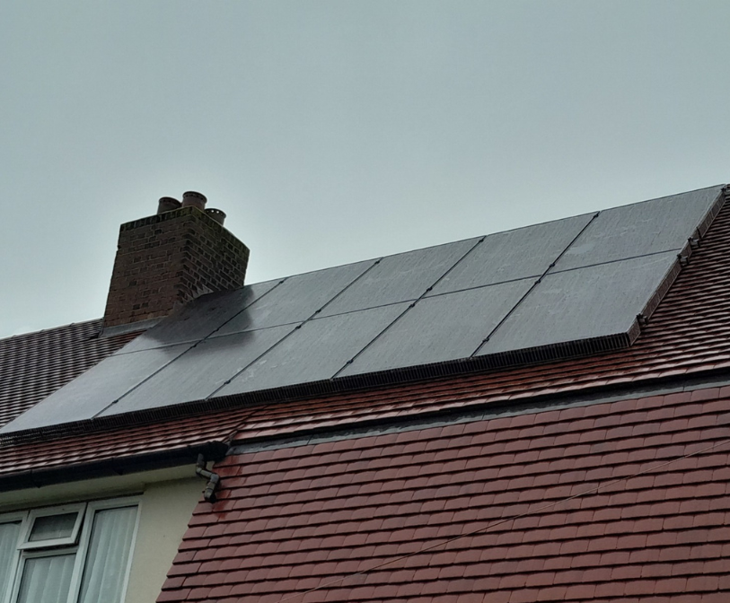 A photograph of solar panels on the roof of a property with cloudy skies above.